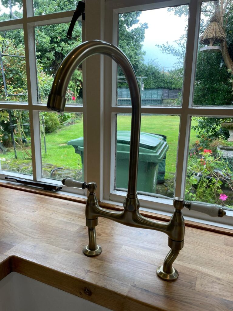 Brushed brass kitchen tap on wooden worktop by window