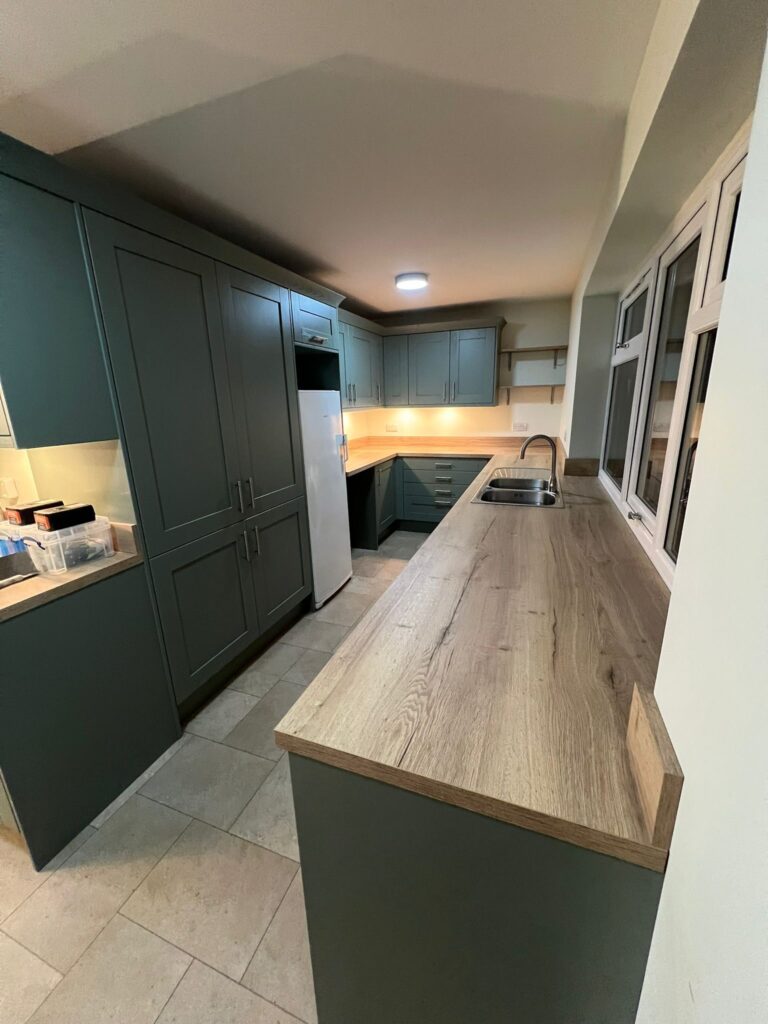 Dark green kitchen cabinetry with wood effect worktop and sink